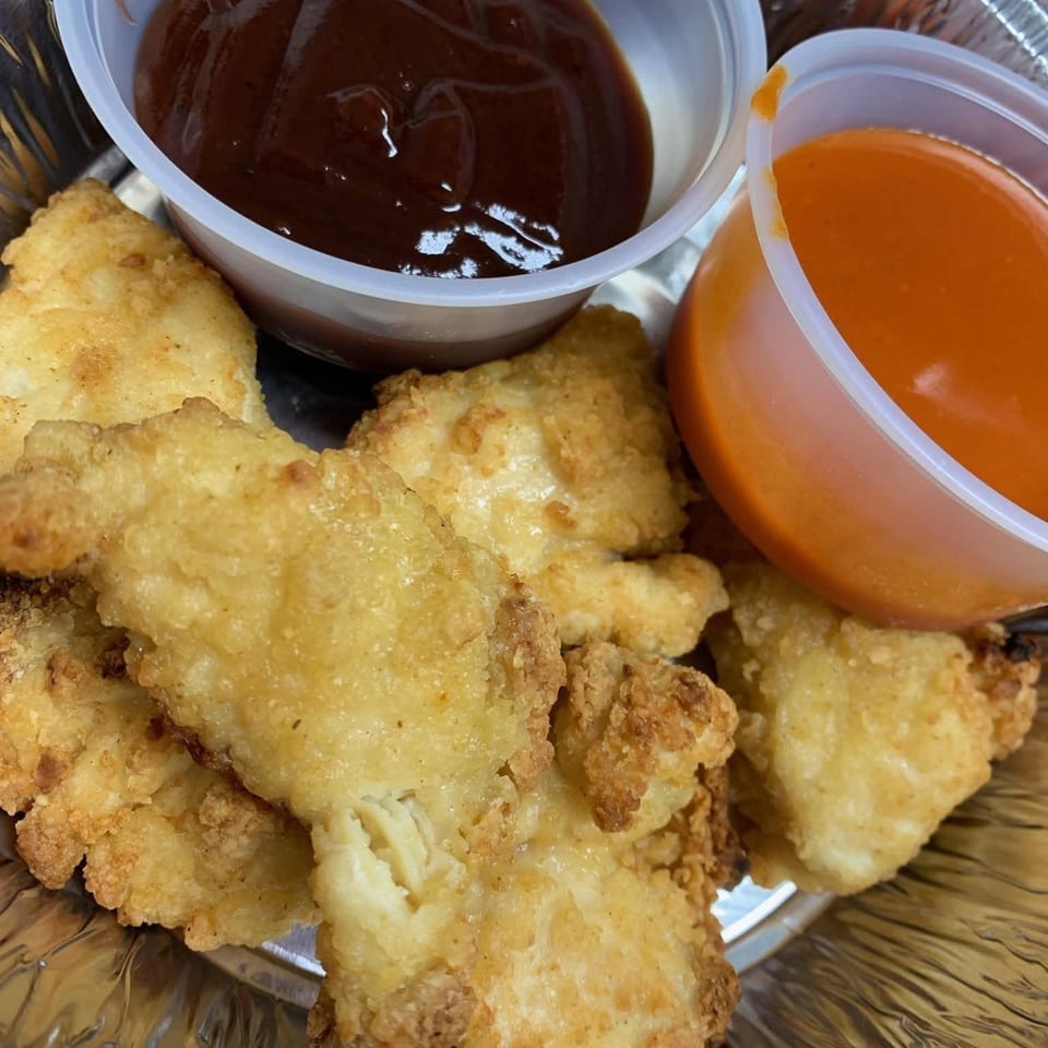 Crispy fried chicken nuggets with two dipping sauces, barbecue and buffalo, in a foil container.