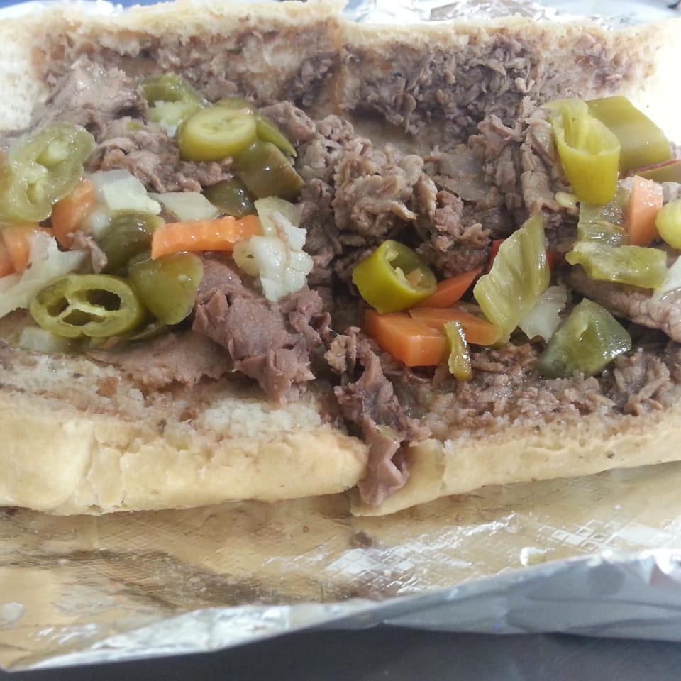 Close-up of a beef sandwich with giardiniera, including peppers, carrots, and onions, on foil.